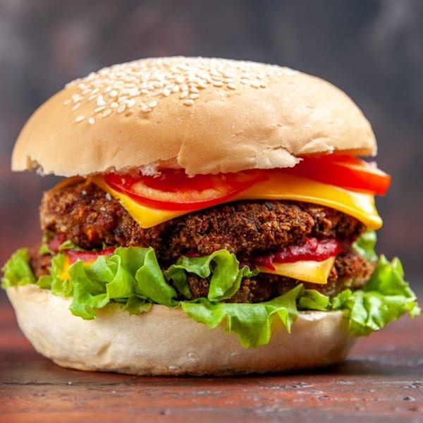 A large burger with two patties, cheese, lettuce, and tomato on a sesame seed bun.