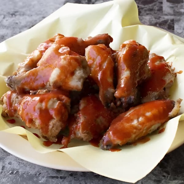 A plate of Wild Pepper Pizza's chicken wings, generously coated in a vibrant red sauce.