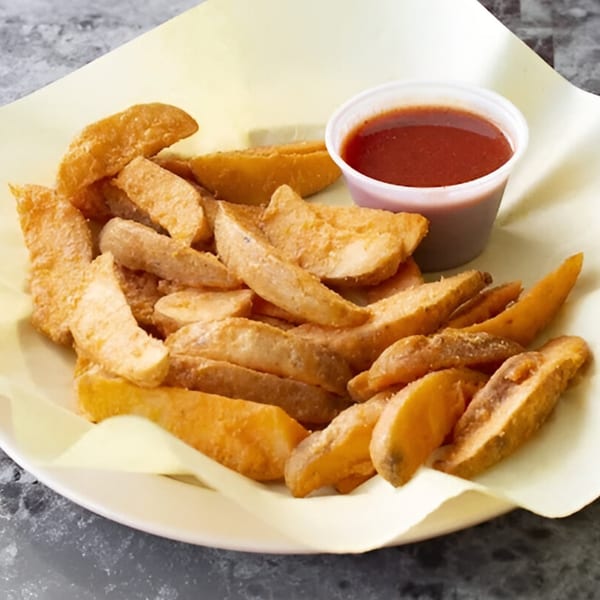 A plate of golden-brown potato wedges with a side of red dipping sauce on a yellow paper liner.
